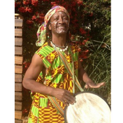 Photo of Baba Shibambo playing a drum and smiling.