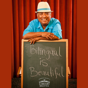 José-Luis Orozco standing in front of a chalkboard that reads: Bilingual is Beautiful.