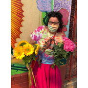 Photo of artist Amanda Ayala holding flowers and wearing a face mask. 