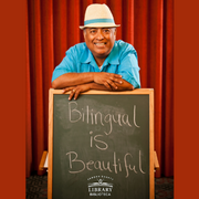 Photo of José-Luis Orozco posing with a chalkboard that reads "Bilingual is Beautiful"