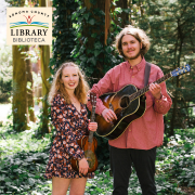 A woman and man holding guitars in a forest 