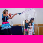 Photo of the Bubble Lady putting 3 children in a giant bubble.