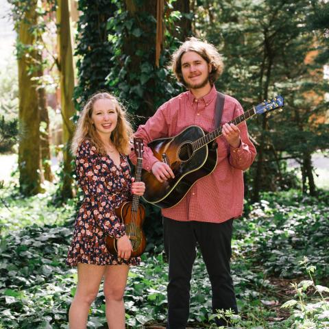 Two people holding a guitar in a forest 